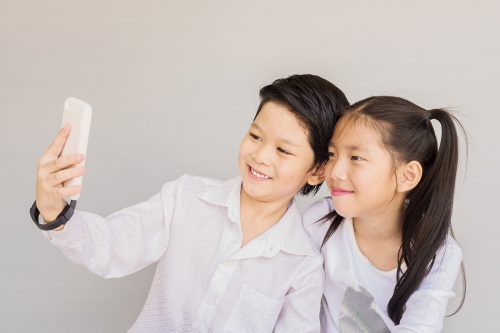 Lovely Asian couple school kids are taking selfie, 7 and 10 years old, over gray background
